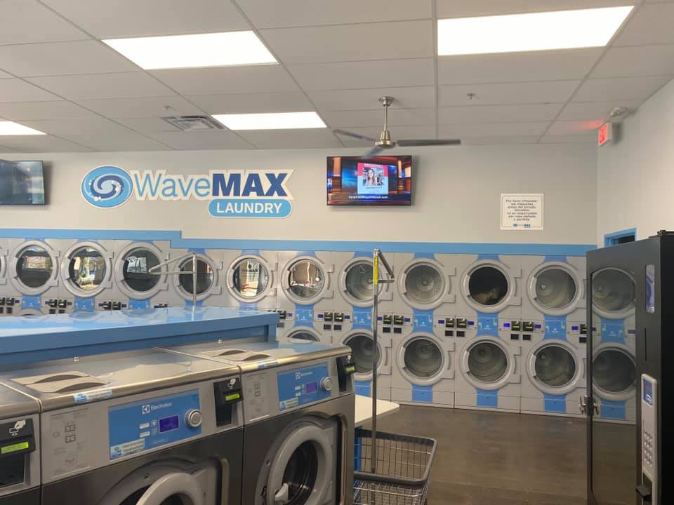 Indoor look at finished WaveMax Laundry business. Wall of dryers with tv overhead. 2 Washing machines to the left.